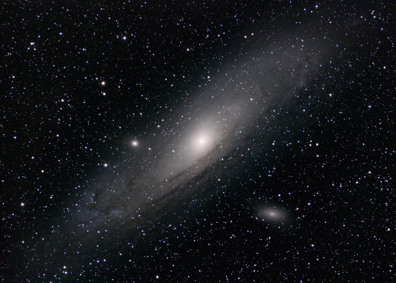 The Andromeda Galaxy seen at an angle, its bright core surrounded by dust lanes; the compact satellite M32 lies just above the core and M110 at lower right.