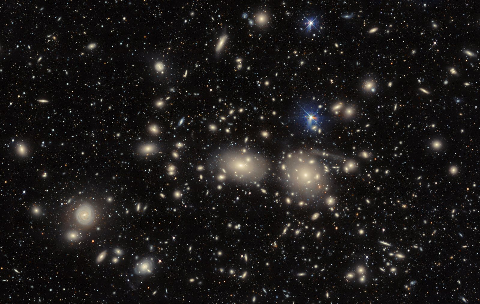 Hundreds of yellowish elliptical galaxies scattered across a dark sky; two giant ellipticals, NGC 4889 and NGC 4874, sit close together near the centre.