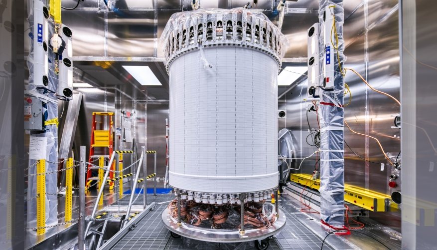 The cylindrical LZ time projection chamber standing in a clean room, wrapped in white panels, with copper cabling visible at its base.