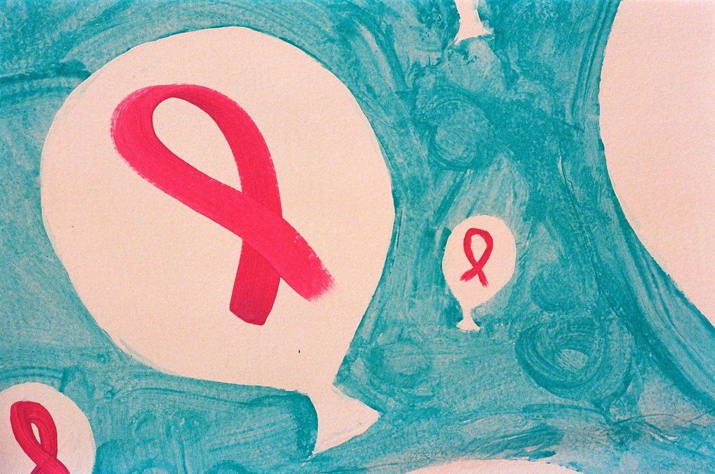 A painted mural of pink awareness ribbons set inside white speech balloons on a teal background.