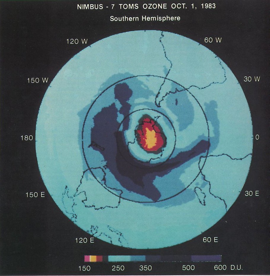A circular map of total ozone over the Southern Hemisphere from Nimbus-7 satellite data, with a small red and yellow area of very low ozone centered on Antarctica.