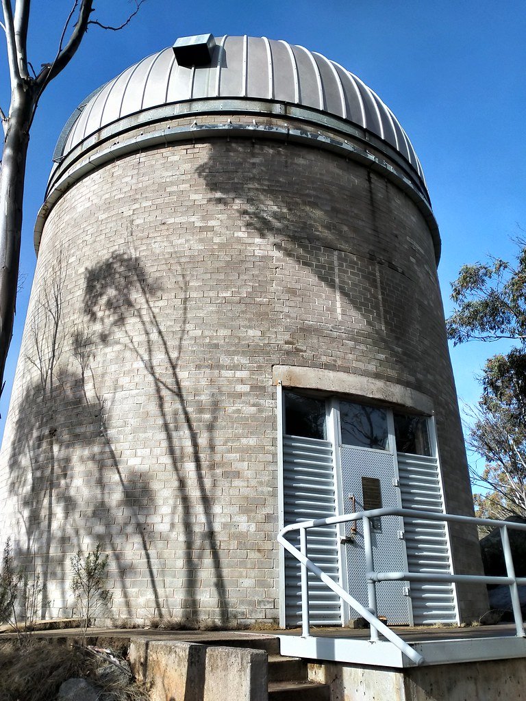 A round brick tower topped by a metal dome, the former Orroral lunar laser ranging building, seen from below against a blue sky.