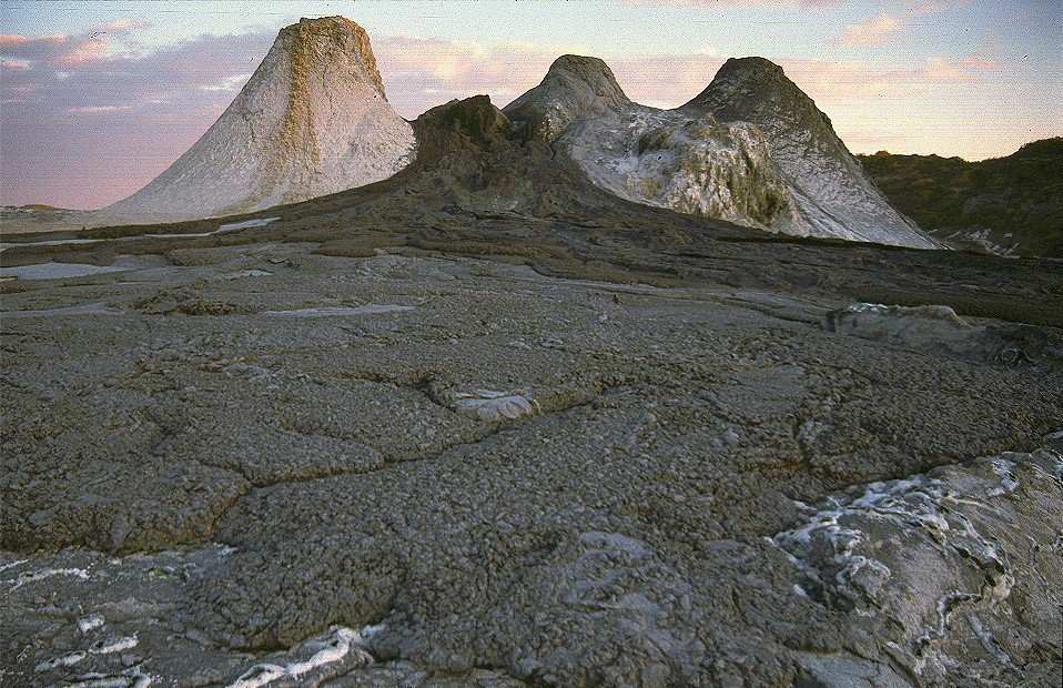 Three small steep-sided spatter cones of pale lava standing on the flat, cracked floor of a volcanic crater at dusk.