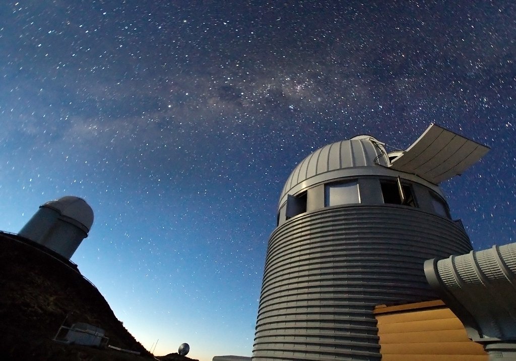 Two telescope domes at La Silla Observatory seen from below against a deep blue twilight sky full of stars.