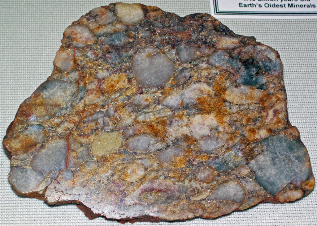 A cut slab of conglomerate rock showing rounded gray and white quartz pebbles set in a rusty orange matrix.