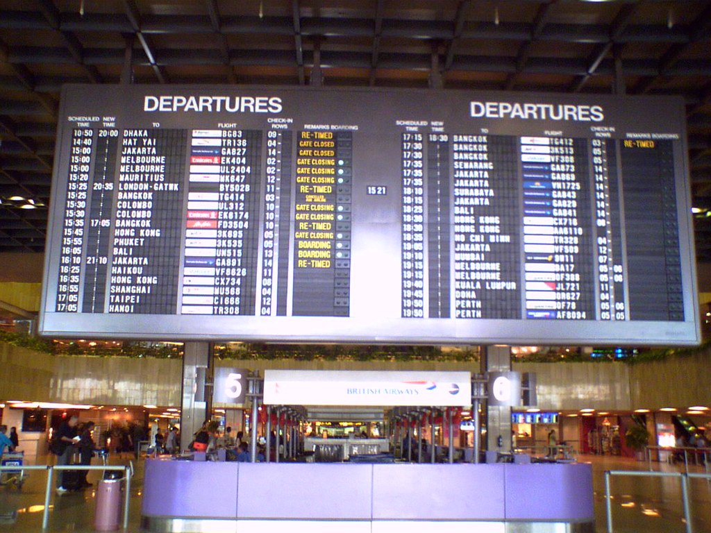 A large departures board in an airport terminal listing flight numbers, destinations and times.