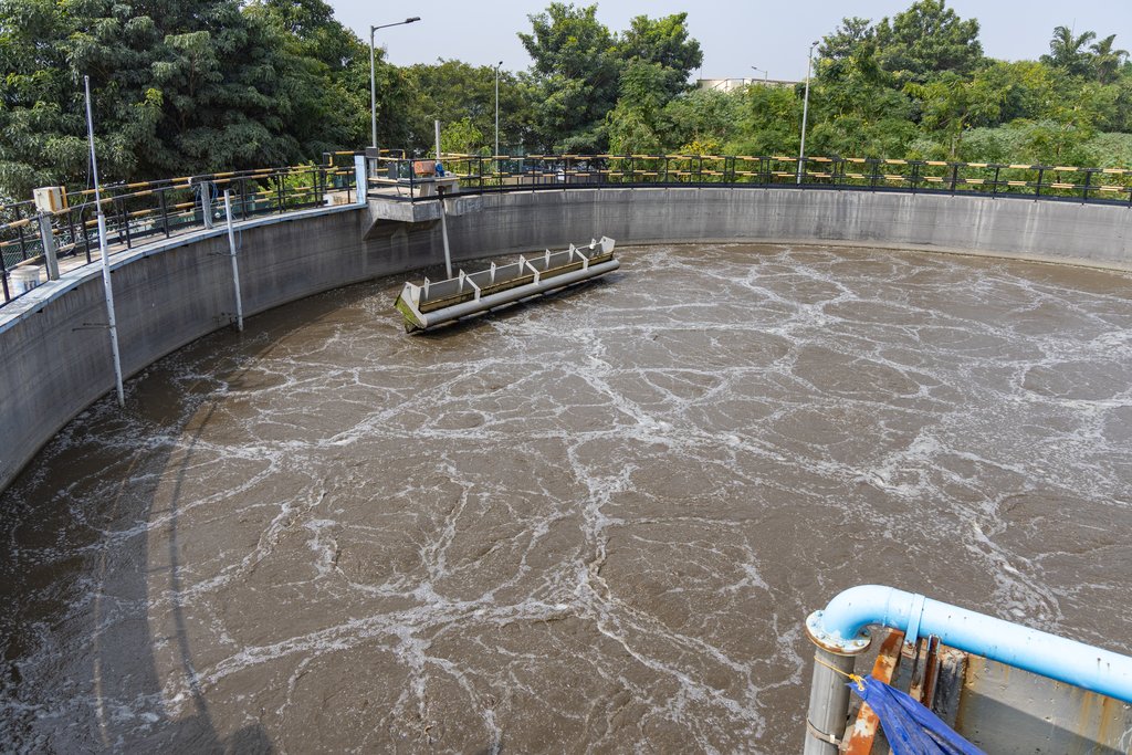 A circular aeration tank at a sewage treatment plant seen from above, its brown surface churning with air.