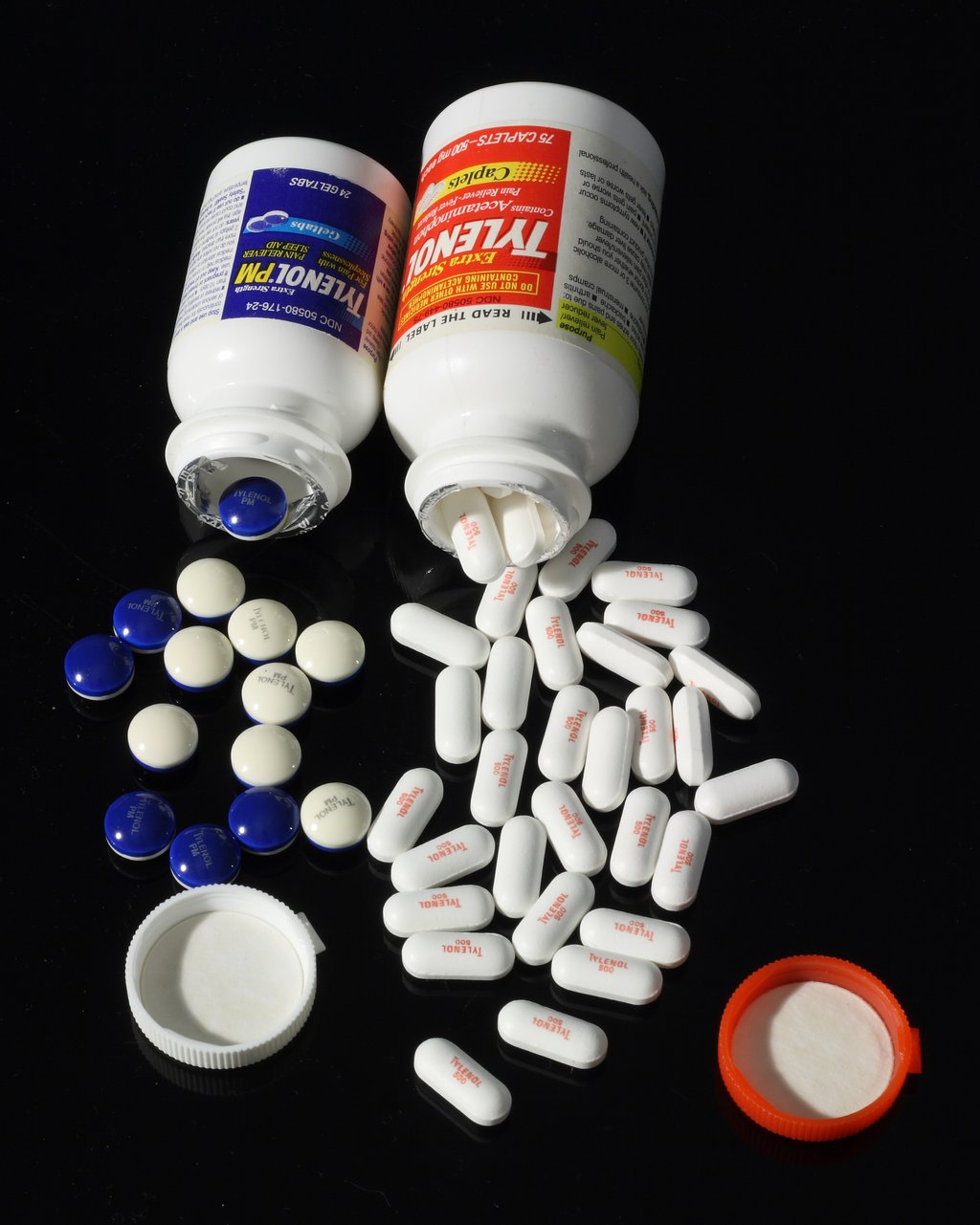 Two opened Tylenol bottles on a black background with white caplets and blue gel tabs spilled in front of them.