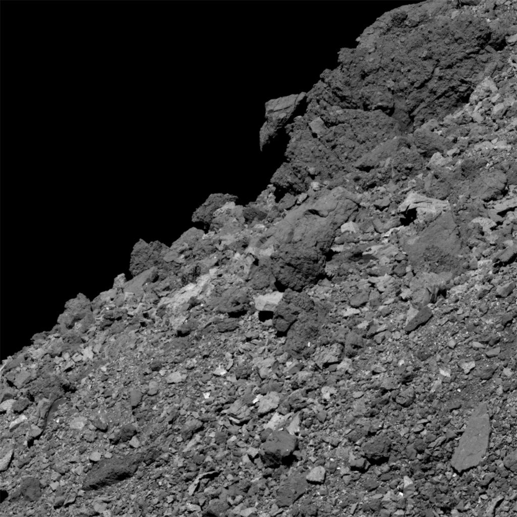 Large angular boulders along the curved edge of asteroid Bennu, set against black space.