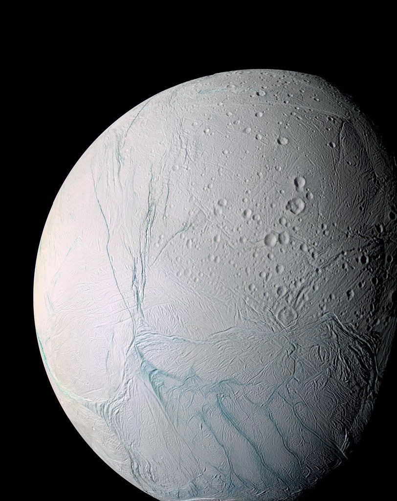 Enceladus in near true color, a white icy globe crossed by blue-green fracture lines and scattered craters.