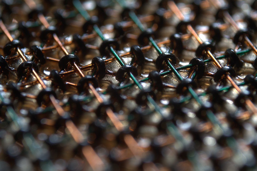 Close-up of magnetic-core memory, with ferrite rings threaded on a crisscross grid of fine copper and green wires.