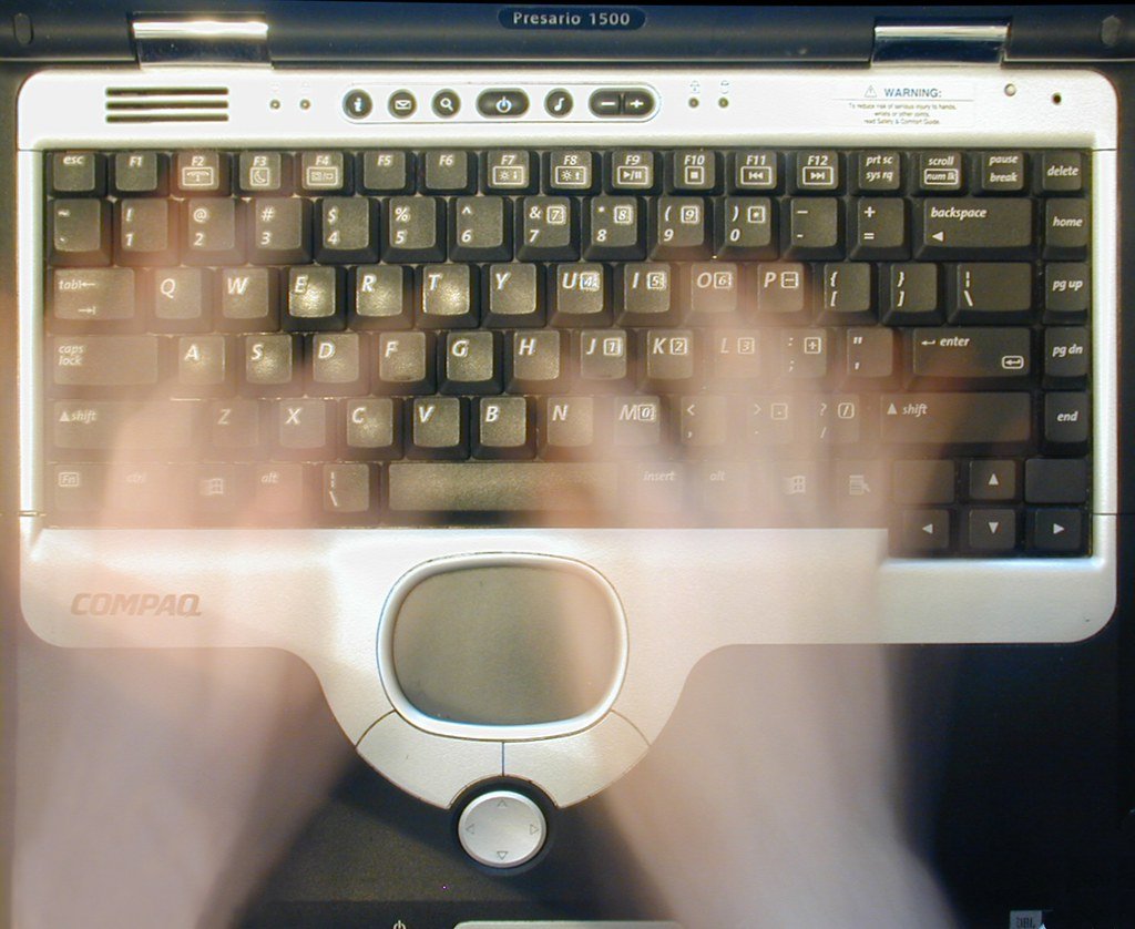 Overhead view of a laptop keyboard with a typist's hands blurred by motion above the keys.