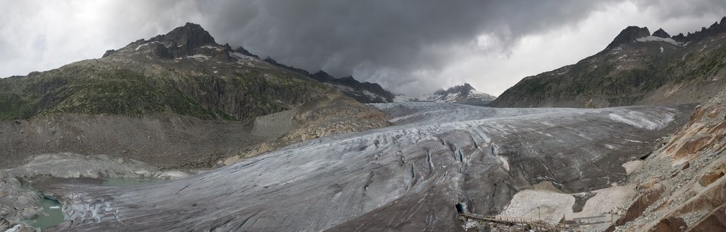 A wide panorama across the debris-streaked surface of the Rhône Glacier, with meltwater pooling at the ice edge on the left.