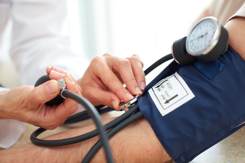 A clinician's hands use an inflatable cuff and a stethoscope to take a seated person's blood pressure.