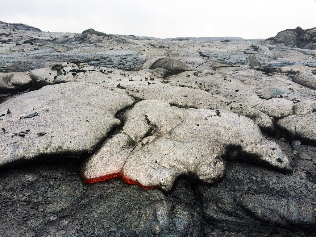 A glowing lobe of pahoehoe lava spreading over hardened black lava on Earth.
