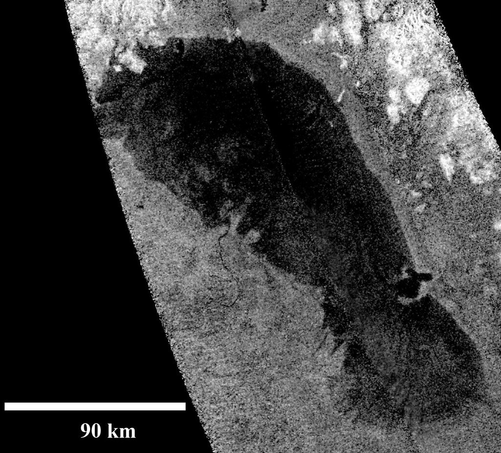 A Cassini radar image of Titan showing a large dark basin against rougher bright ground, with a 90 kilometer scale bar.
