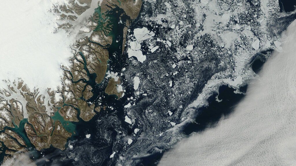 Satellite view of floes and open water along a snow covered coastline, with cloud bands offshore.
