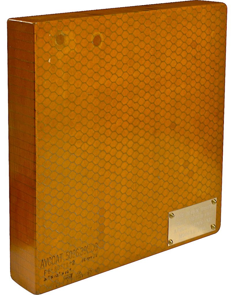A square orange panel whose face is a dense grid of small honeycomb cells filled with ablative material, with a stenciled part number along the bottom edge.