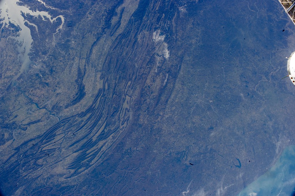Oblique photograph from the International Space Station showing long parallel mountain ridges under a blue haze.