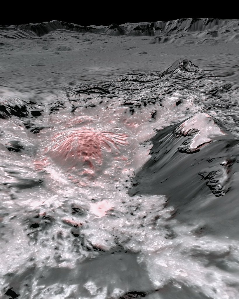 An oblique, enhanced-color view across the floor of Occator Crater on Ceres, showing a pale pink and white dome of salt deposits surrounded by gray rubble and crater walls.