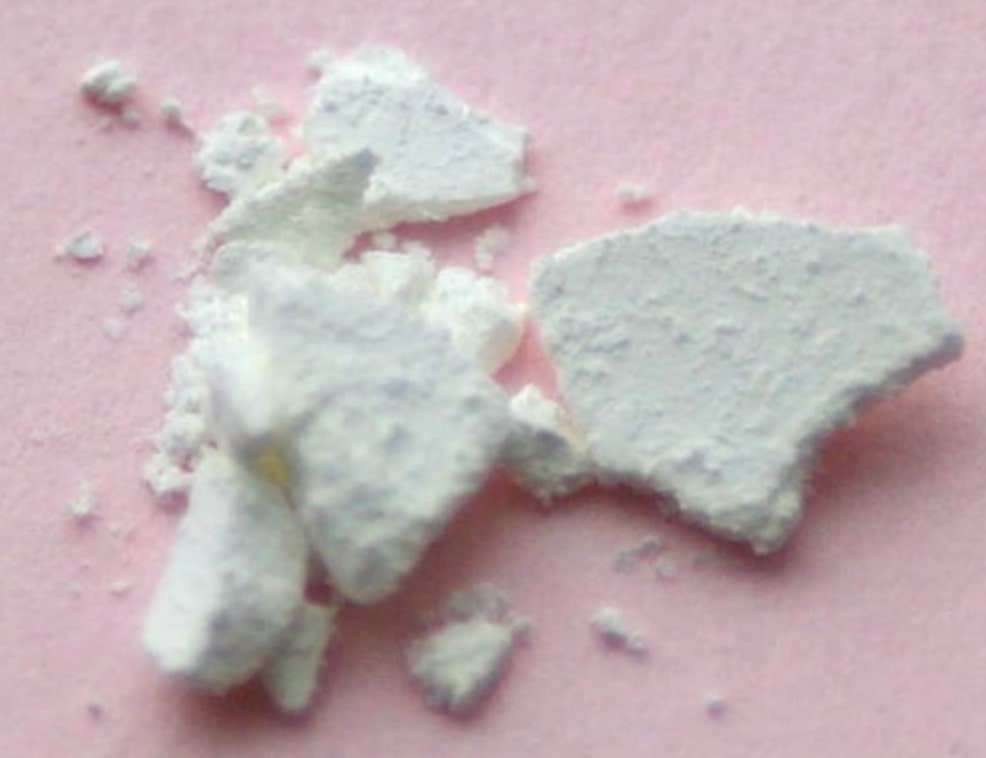 Flakes and crumbs of white dysprosium oxide powder on a pink surface.