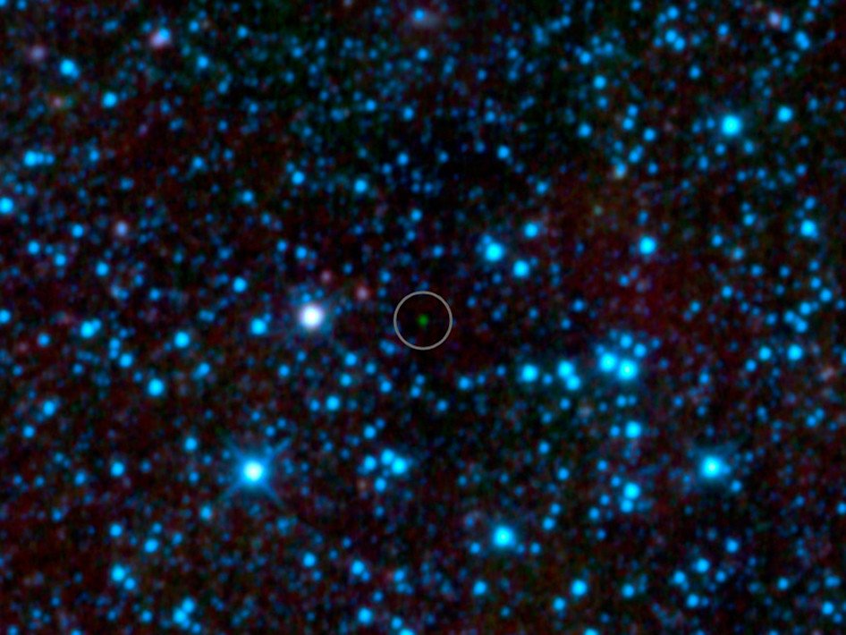 An infrared survey image speckled with blue points of light; a faint green point at the center is marked with a circle.