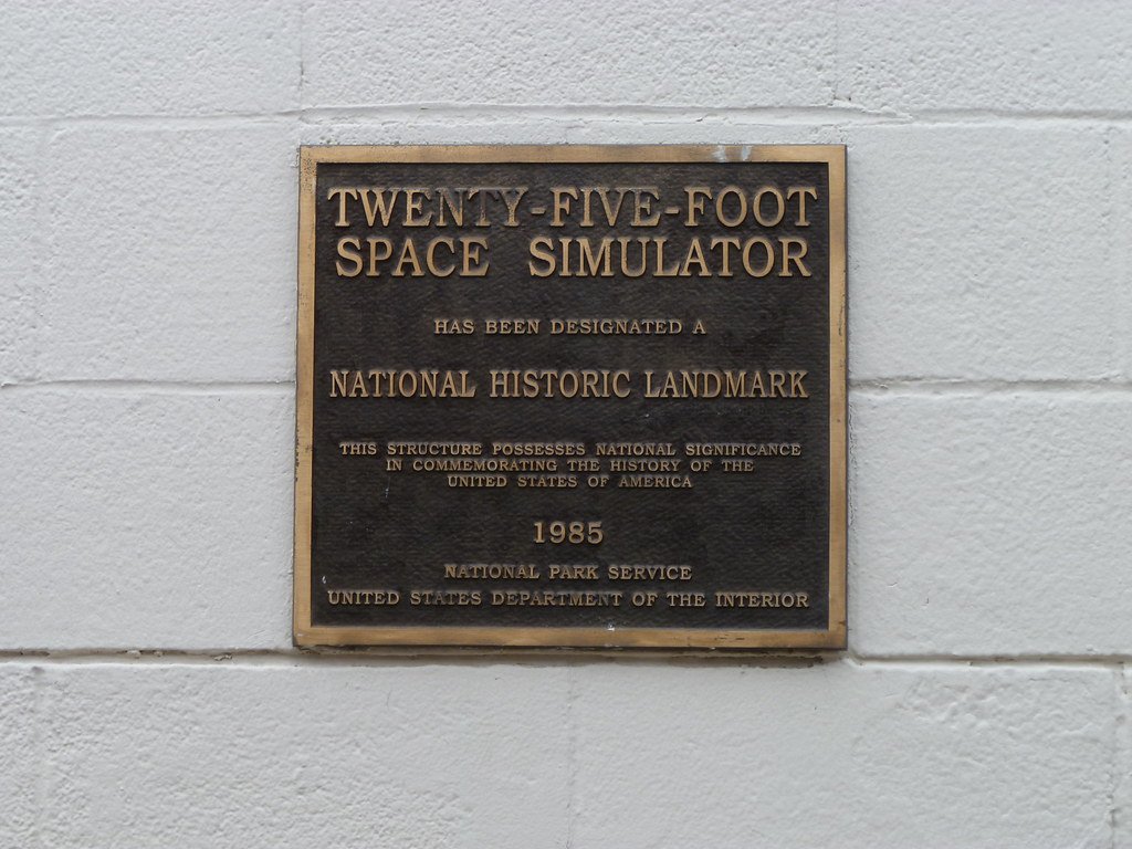 A bronze plaque on a white brick wall reading Twenty-Five-Foot Space Simulator has been designated a National Historic Landmark, 1985, National Park Service.