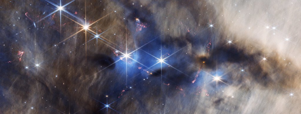 A near-infrared panorama of a dusty cloud north of the Orion Nebula, with blue haze, dark dust lanes, small red arcs of gas thrown out by forming stars, and bright spiked stars.