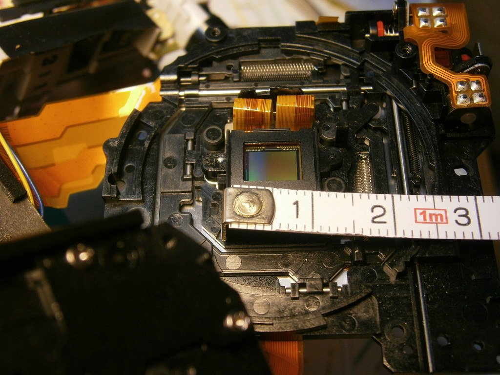 A tape measure marked in centimeters laid across the inside of an opened camera, just below the sensor.
