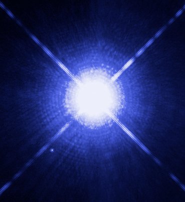A Hubble telescope image of the star Sirius: a brilliant blue-white point with four diffraction spikes, and a much fainter dot below and to the left of it, the white dwarf Sirius B.