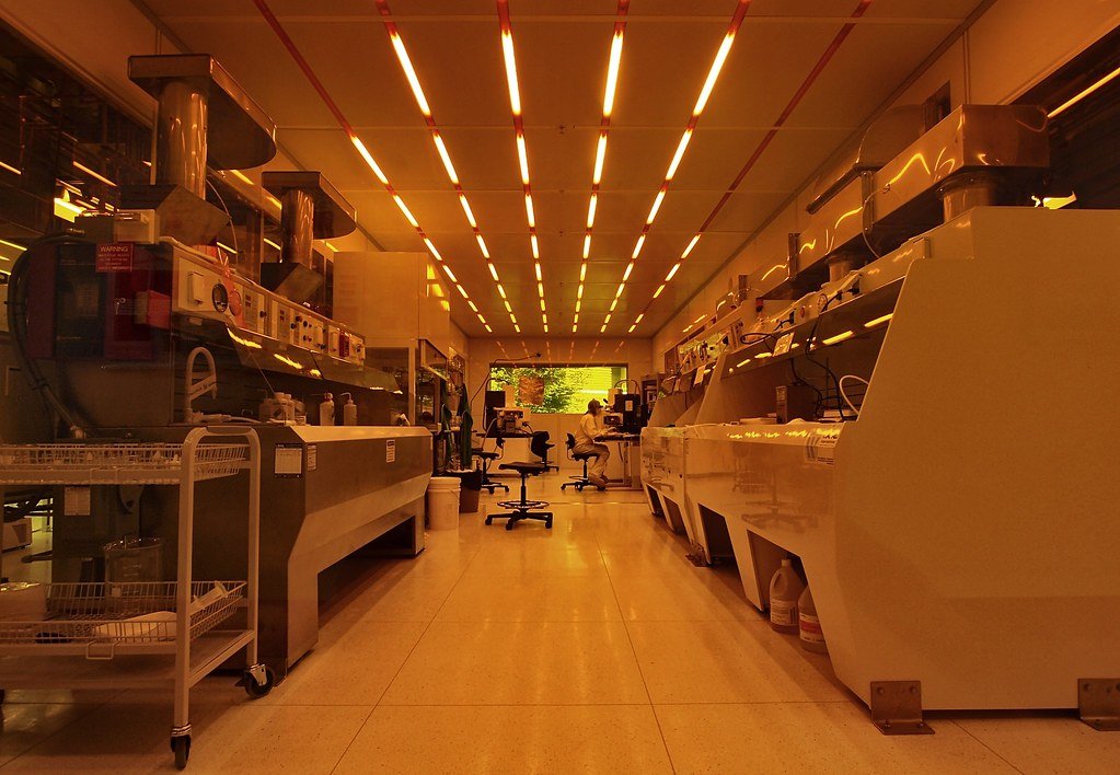 A long cleanroom corridor lit in yellow, lined with wet-process benches and fume hoods.