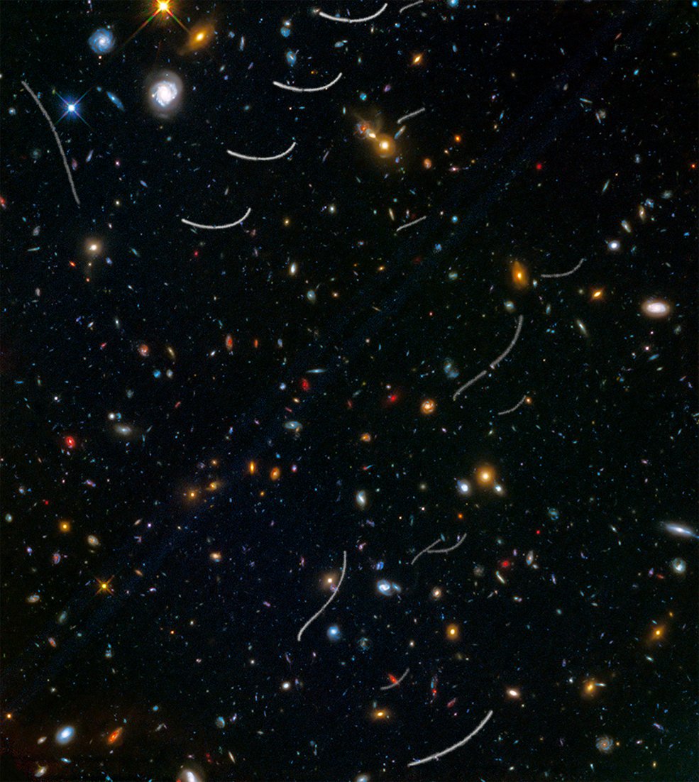 A deep field of galaxies crossed by several short white curved streaks left by nearby asteroids.