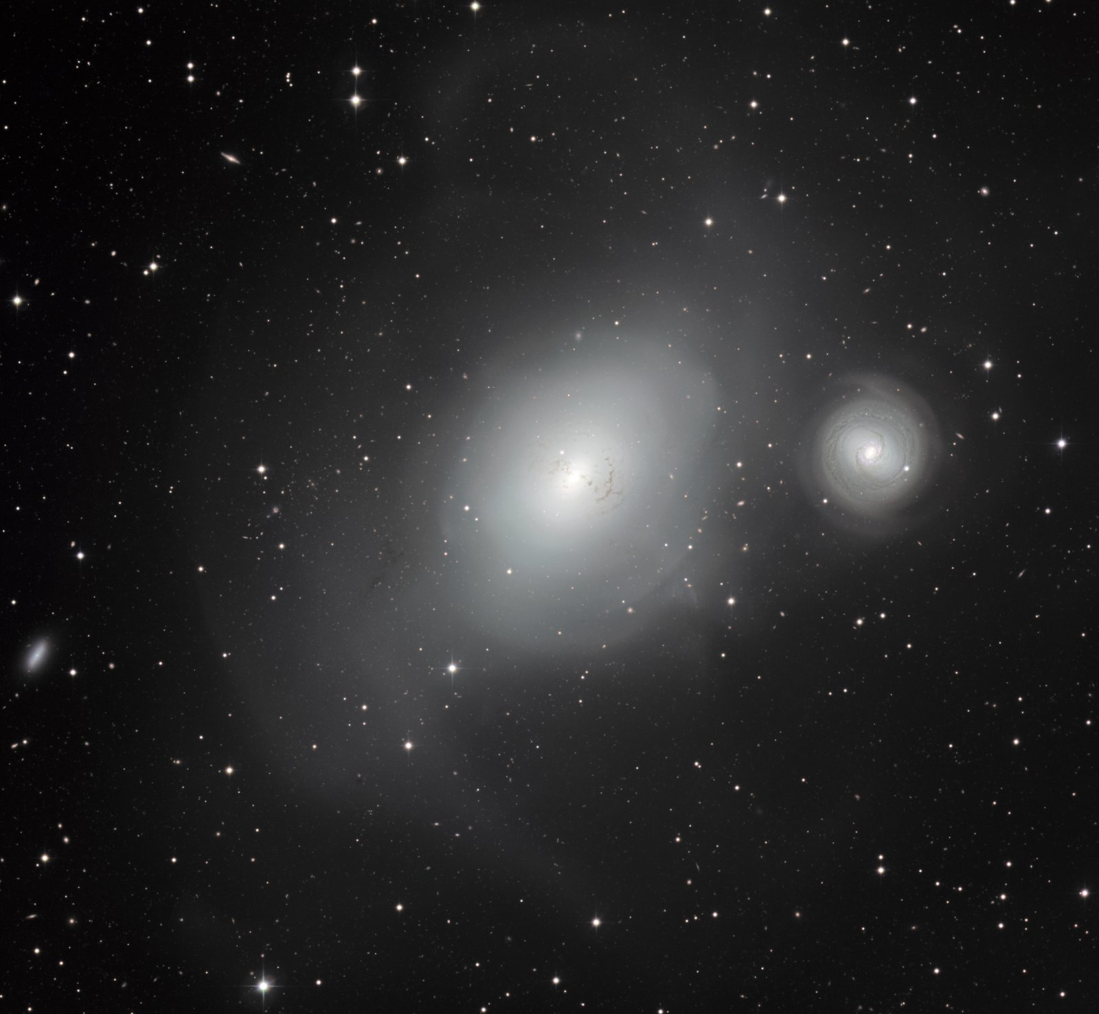 A large diffuse elliptical galaxy beside a smaller spiral galaxy at right, both set in a star field.