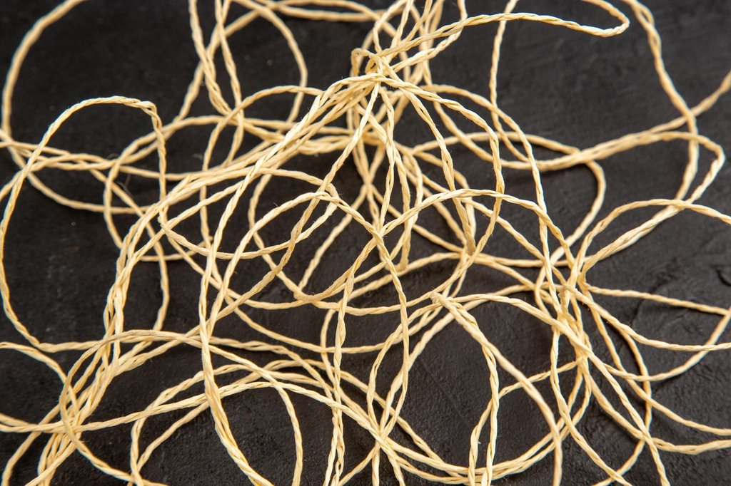 Thin pale twine strewn in loose loops across a dark stone surface, the strands crossing over one another many times.