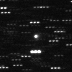 A small square telescope frame in which most stars appear as triplets of dots, while one round point of light near the center stays single.