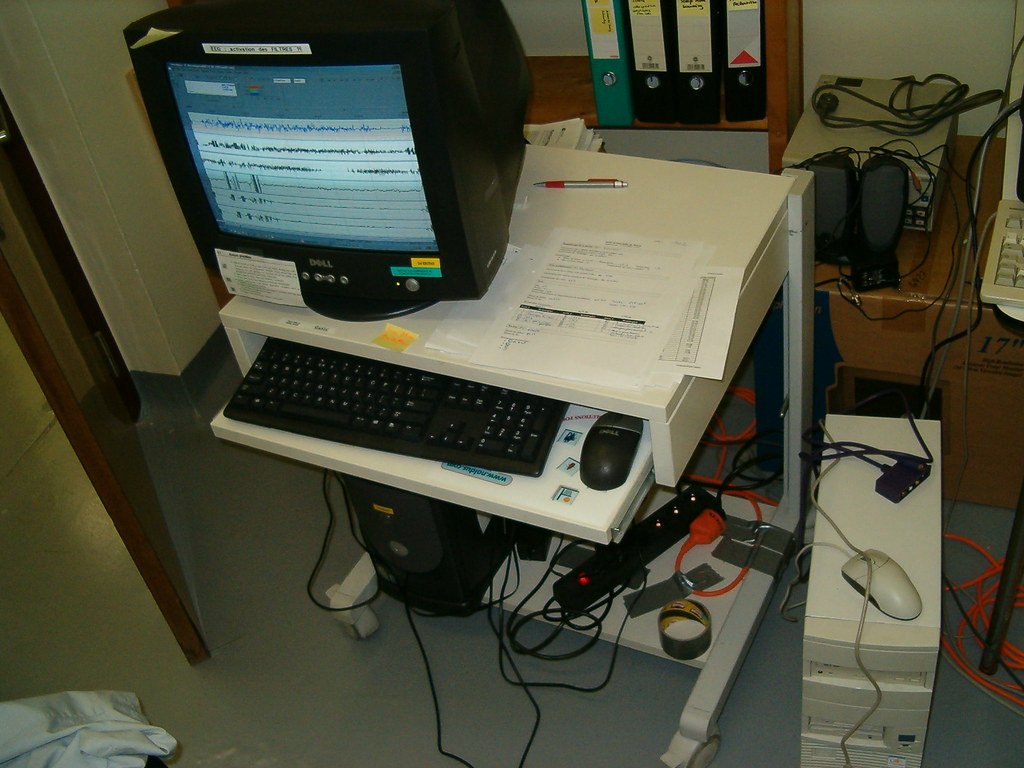 A recording cart in a sleep laboratory, with a computer monitor showing scrolling traces of breathing and brain activity.