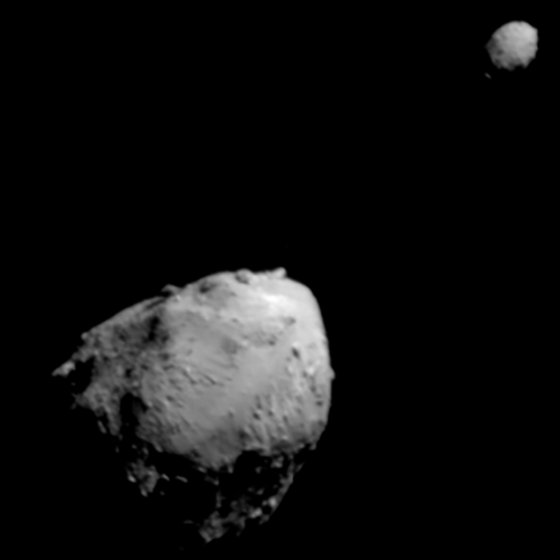 A gray angular asteroid at lower left and a much smaller rounded asteroid at upper right, against black space.