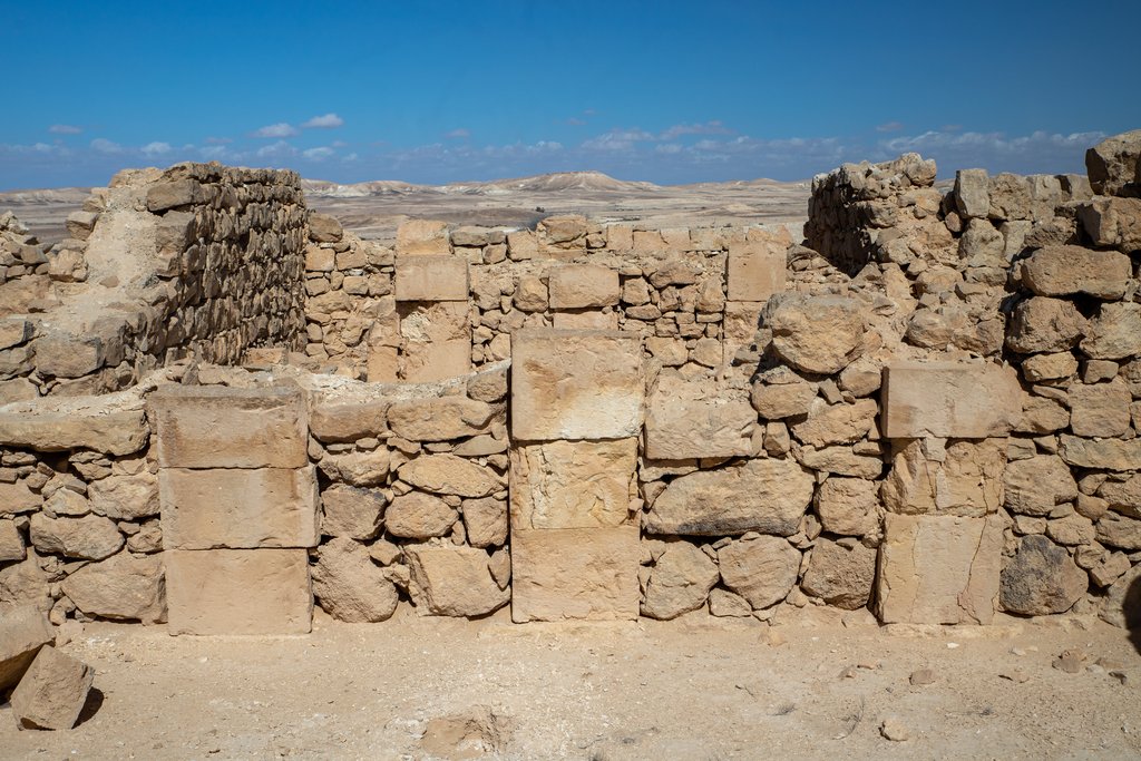 A single wall face seen straight on, mixing tall squared blocks with courses of smaller rough stones, with open desert and low hills visible beyond it.
